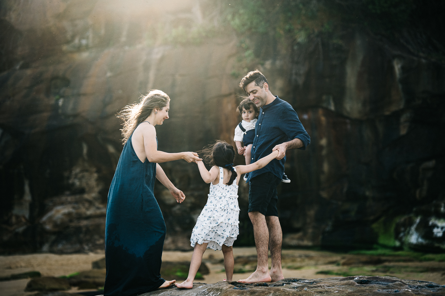 Young family helping each other to climb rocks at the beach during sunset