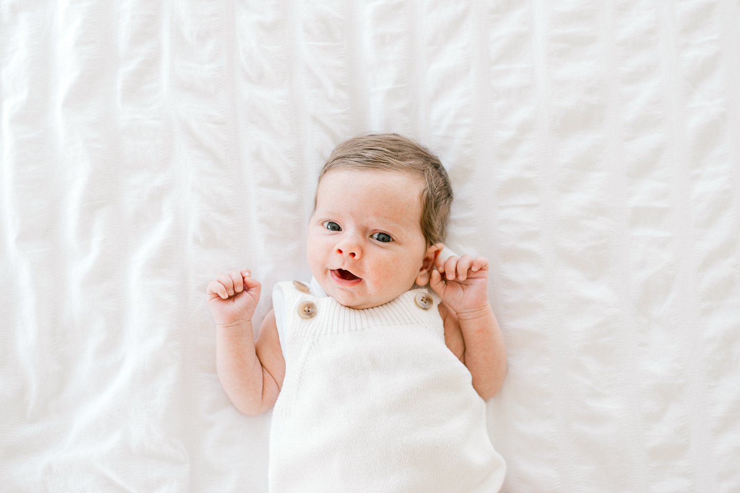 Newborn baby lying on bed wearing a knitted overall and making faces