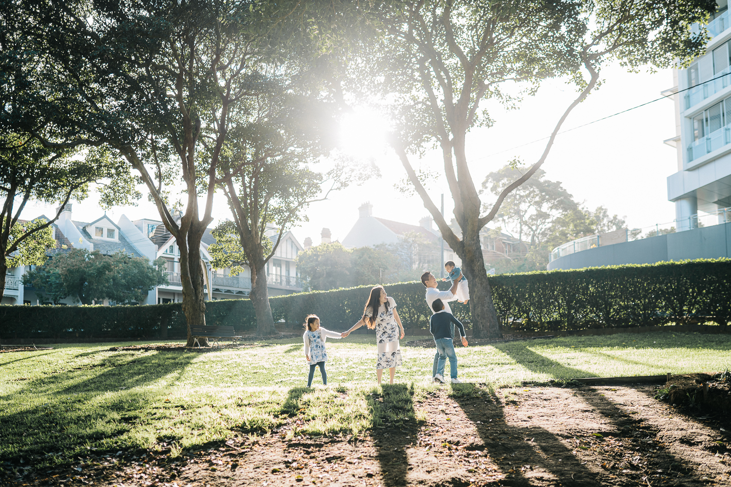 joyful family of five playing in the garden backlit by the sun