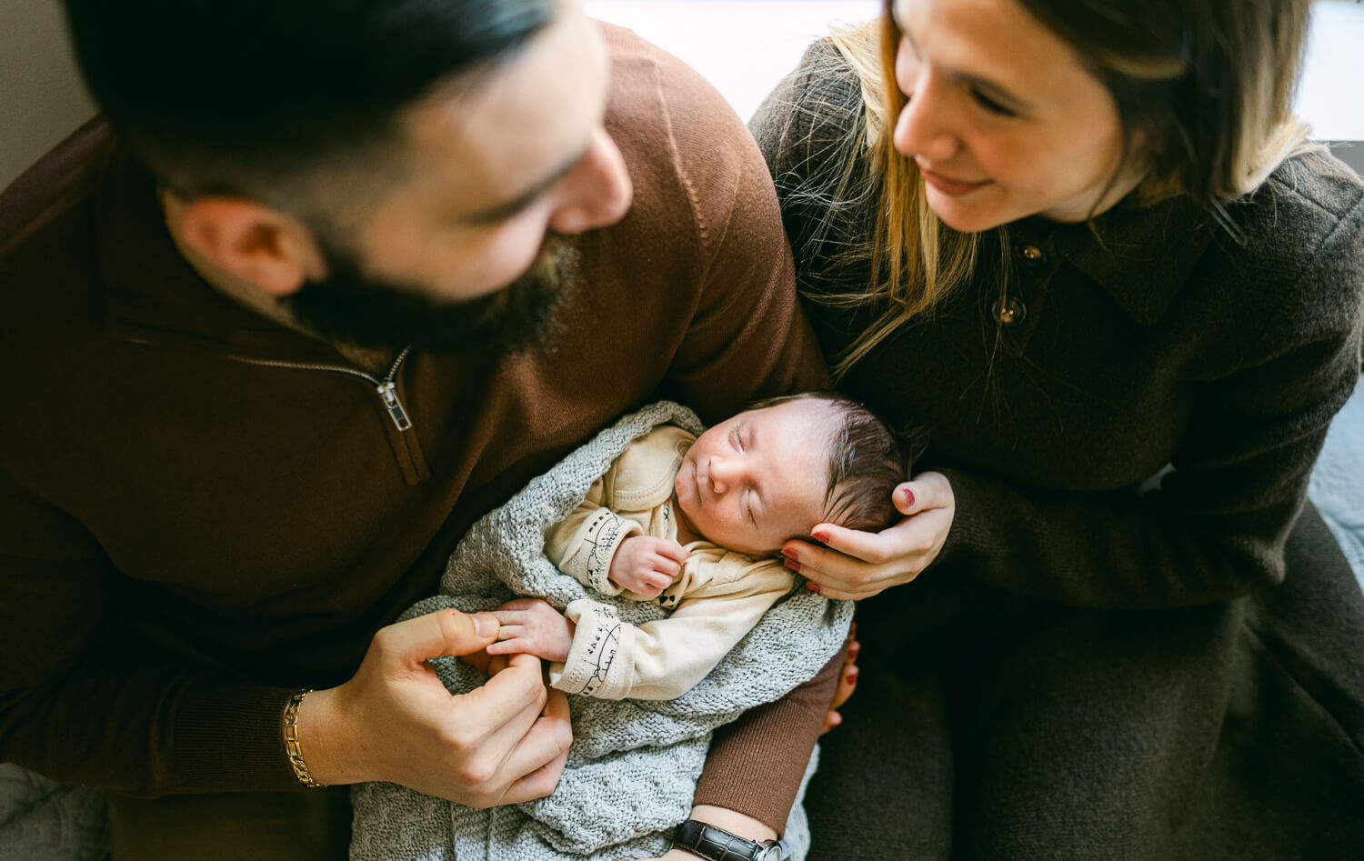 Newborn baby cradled in parents hand while sitting down against the window