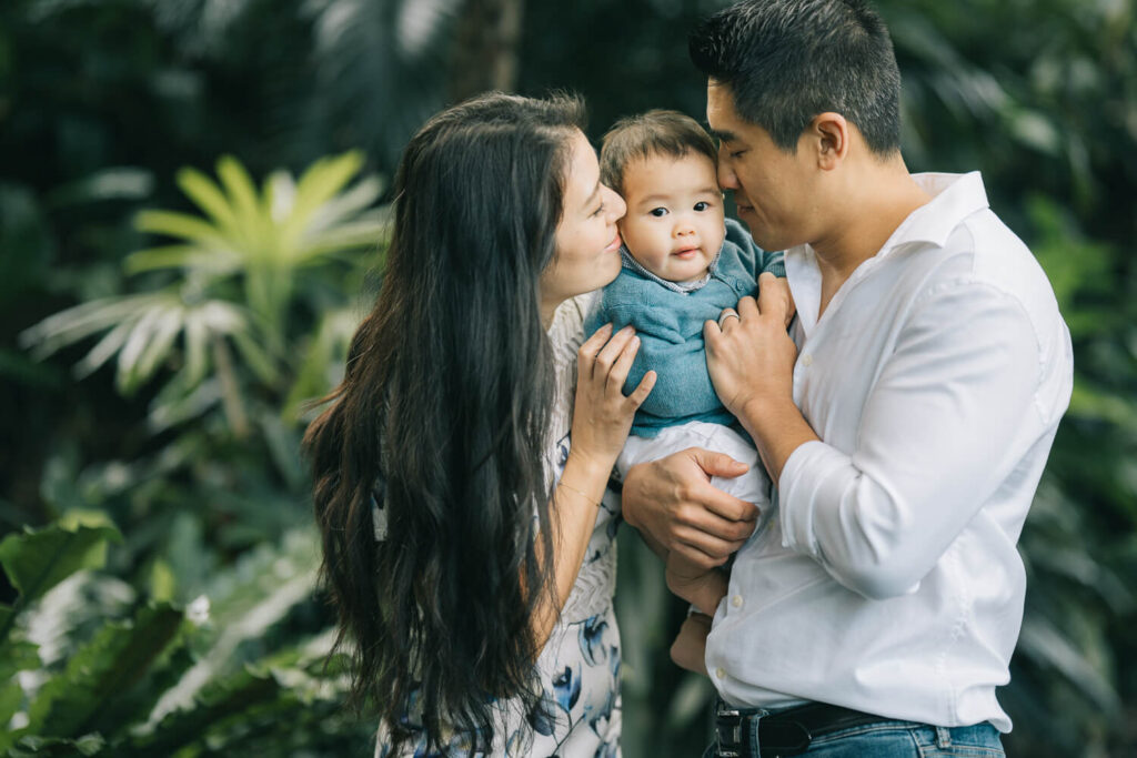 mum and dad kissing baby's cheek in a serene Sydney garden