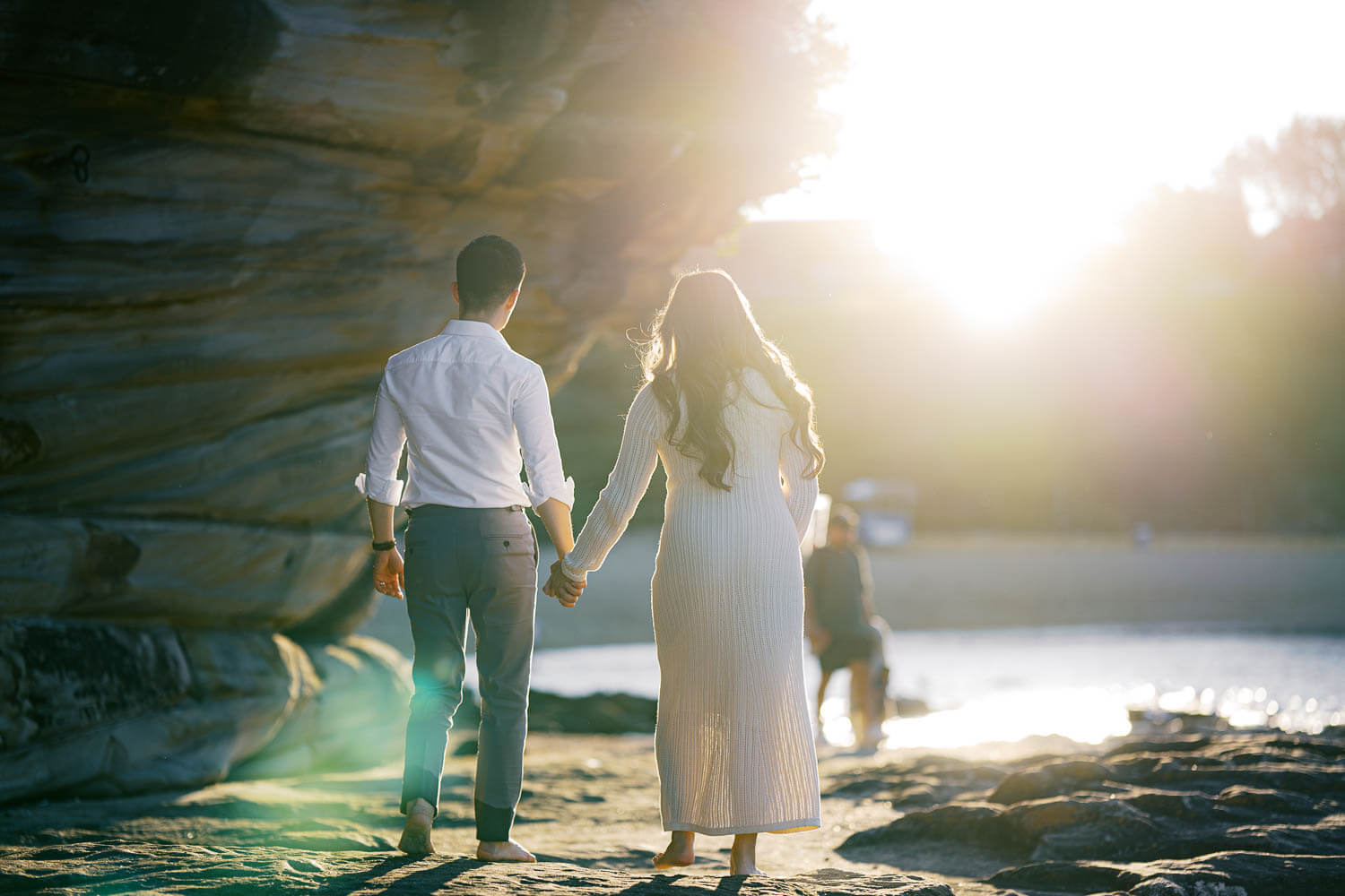 Expecting parents walking hand in hand towards sunset, back facing, at the beach