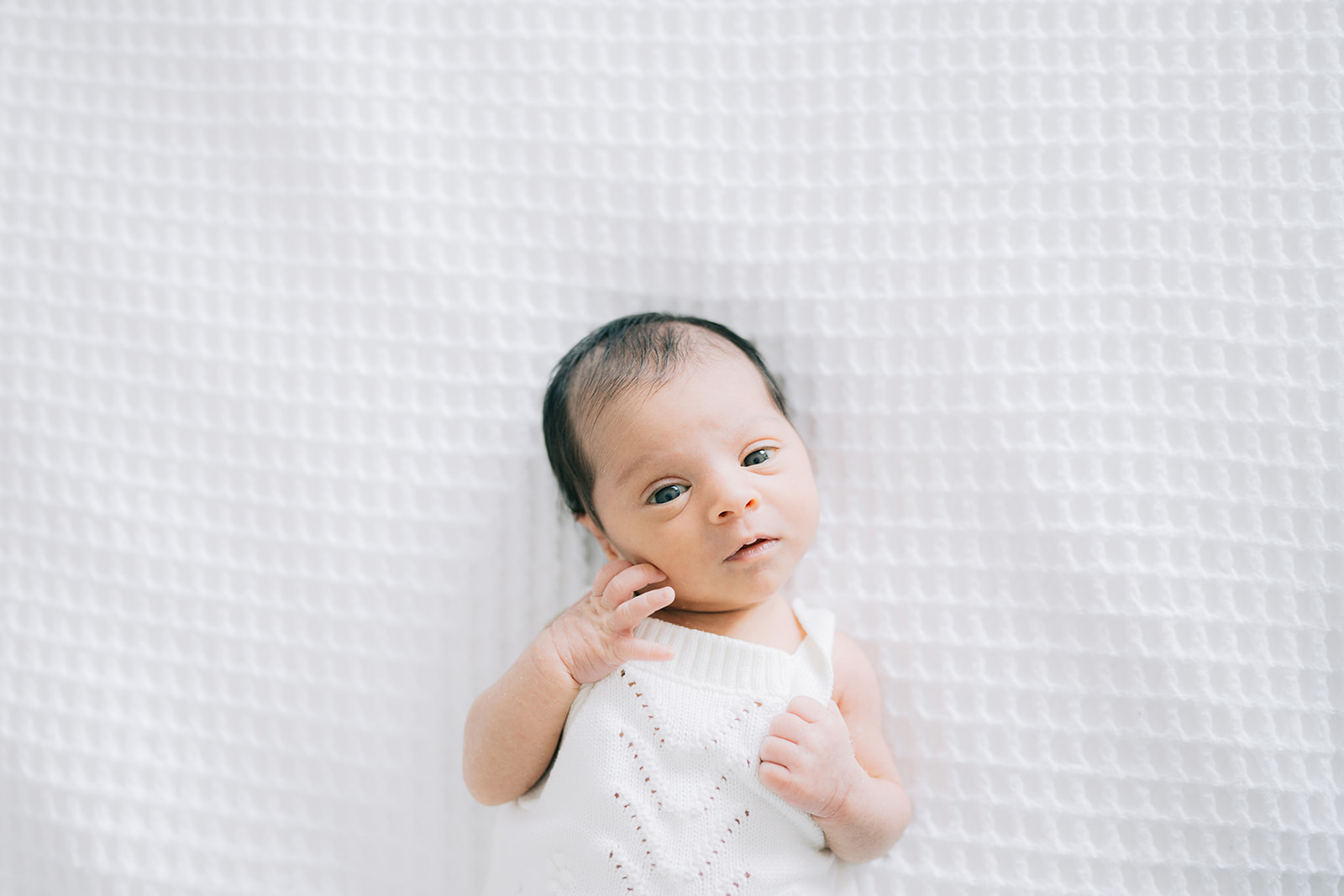 Close up portrait of newborn baby laying flat on white bedsheet