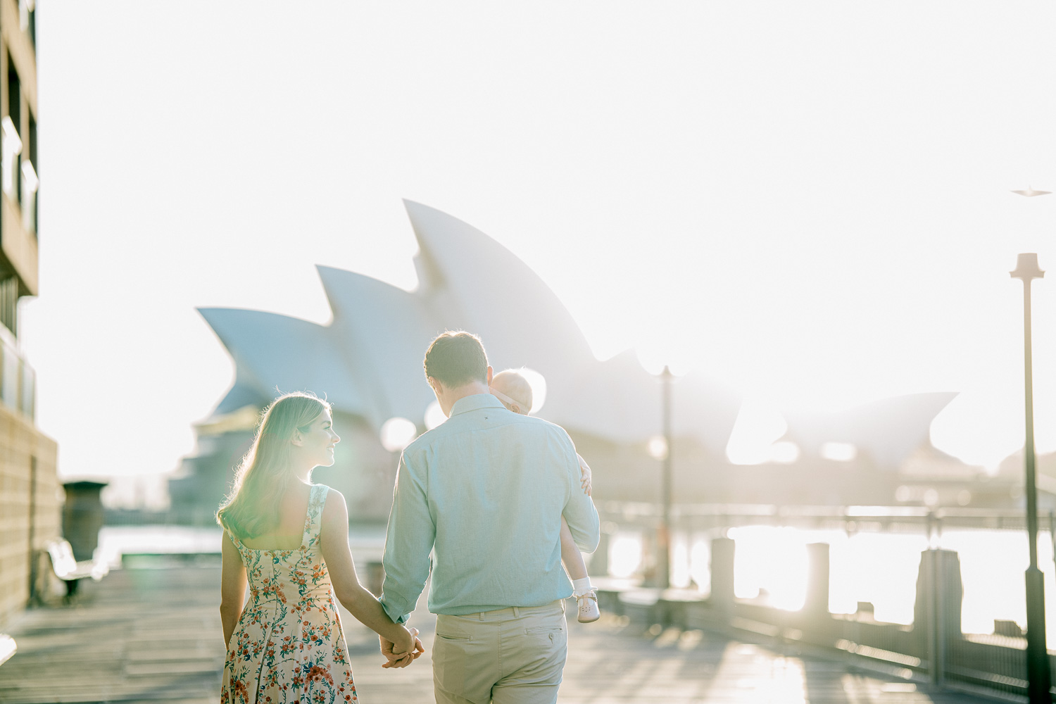Family of three strolling during sunrise with Opera House behind them
