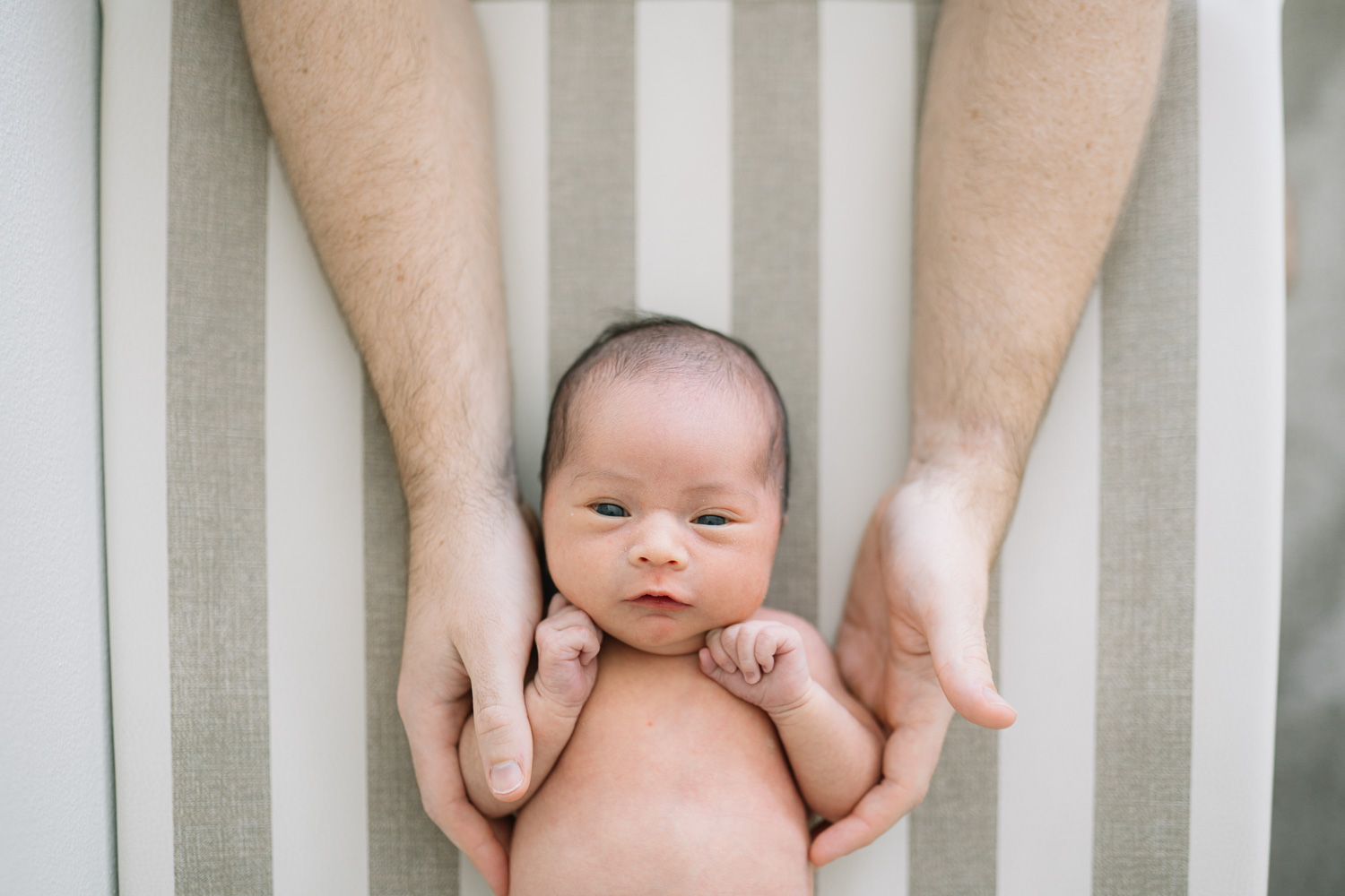 Close up portrait of newborn baby lying down and supported by parents hands.