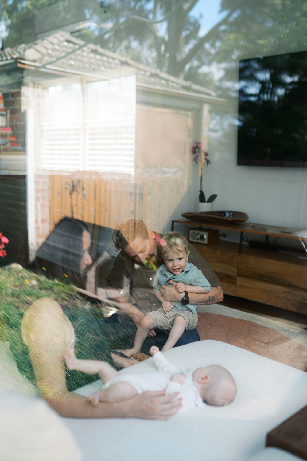 Home life with a newborn baby and a toddler captured from outside the window of home.