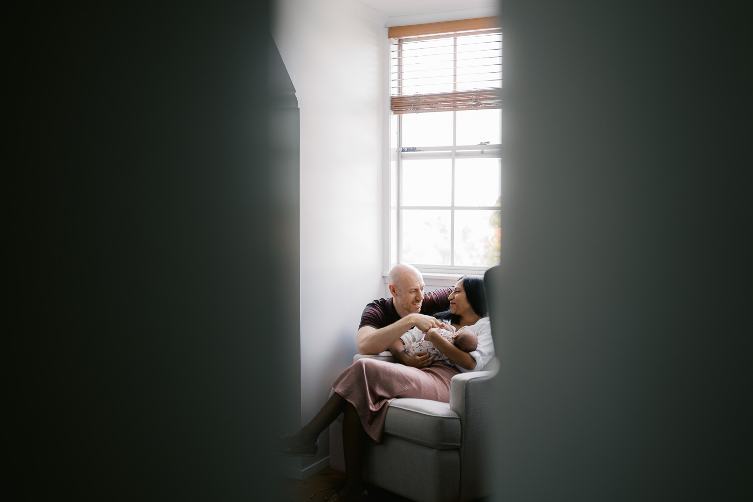 A peek of new parents cradling their newborn baby inside their home
