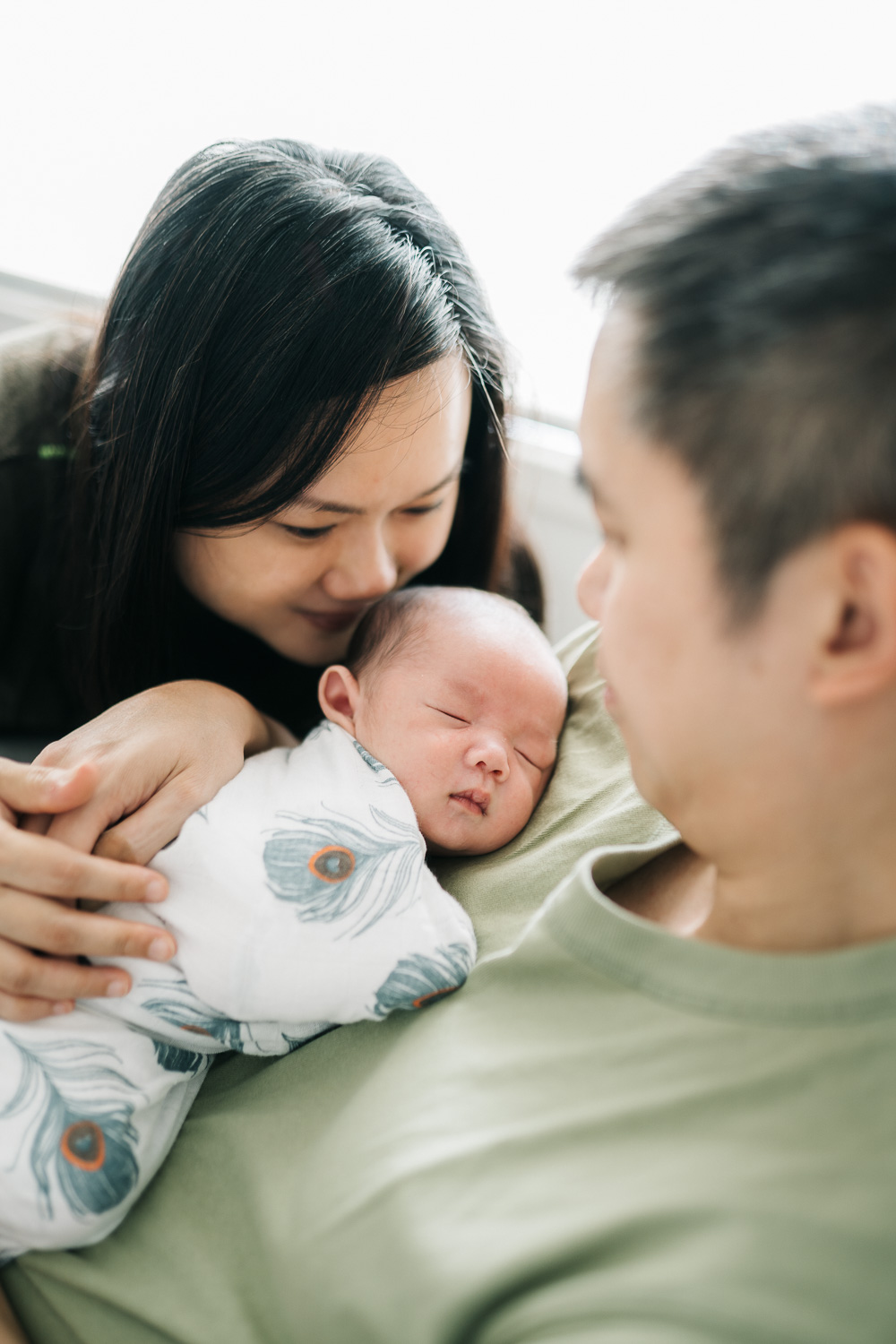 Newborn baby resting on dad's chest while being dote on by mum